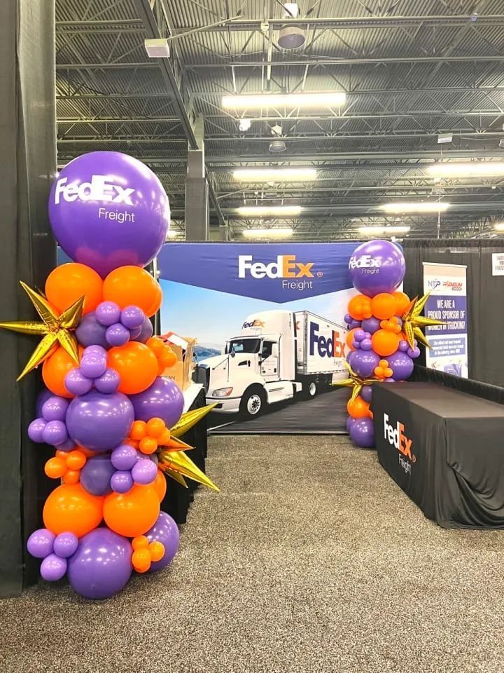 FedEx Freight display at an event, featuring purple and orange balloon columns and a backdrop with a truck.