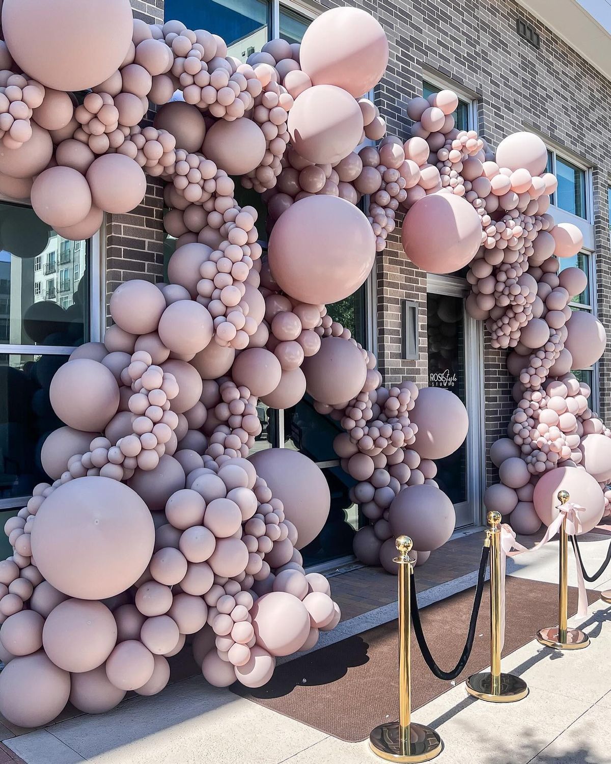 A bunch of pink balloons are hanging from the side of a building.