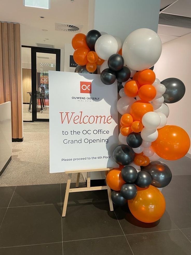 A welcome sign is surrounded by balloons in a room.