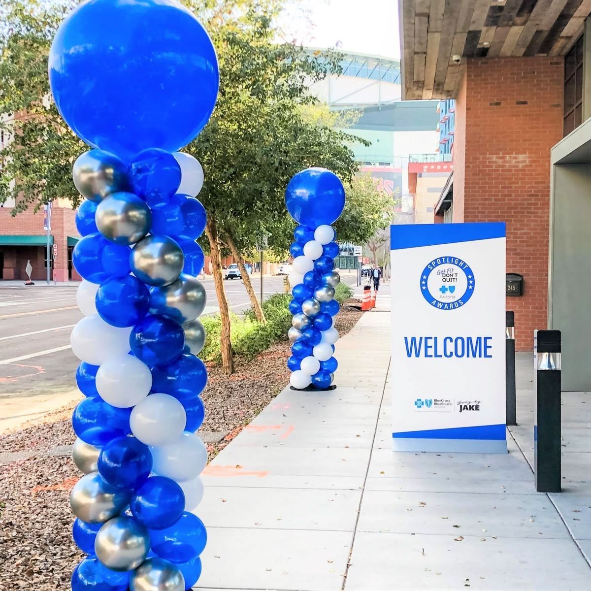 Balloons and welcome sign outside a building. Blue, white, and silver balloons decorate columns.