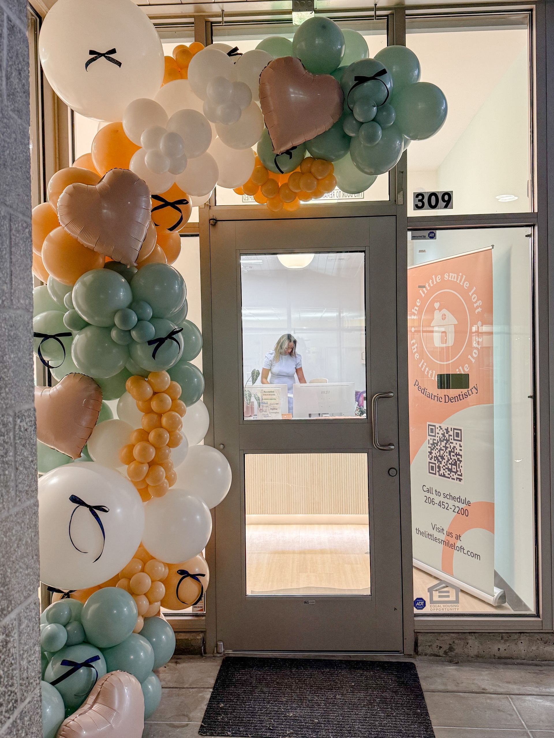 A woman is standing in front of a door decorated with balloons.