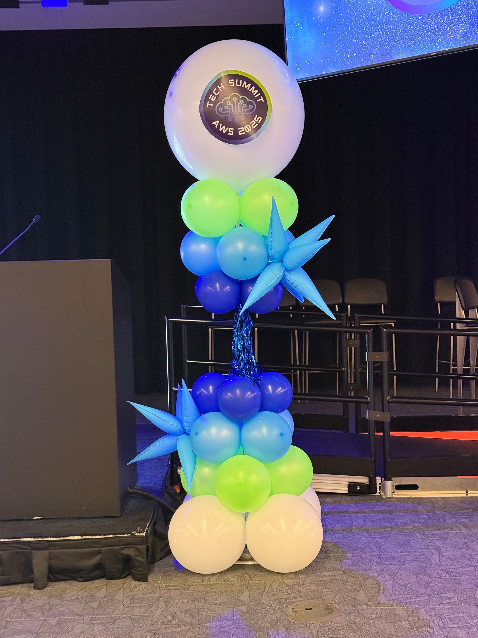 Balloon column in blues, greens, and white, with starbursts and a top balloon with a logo.