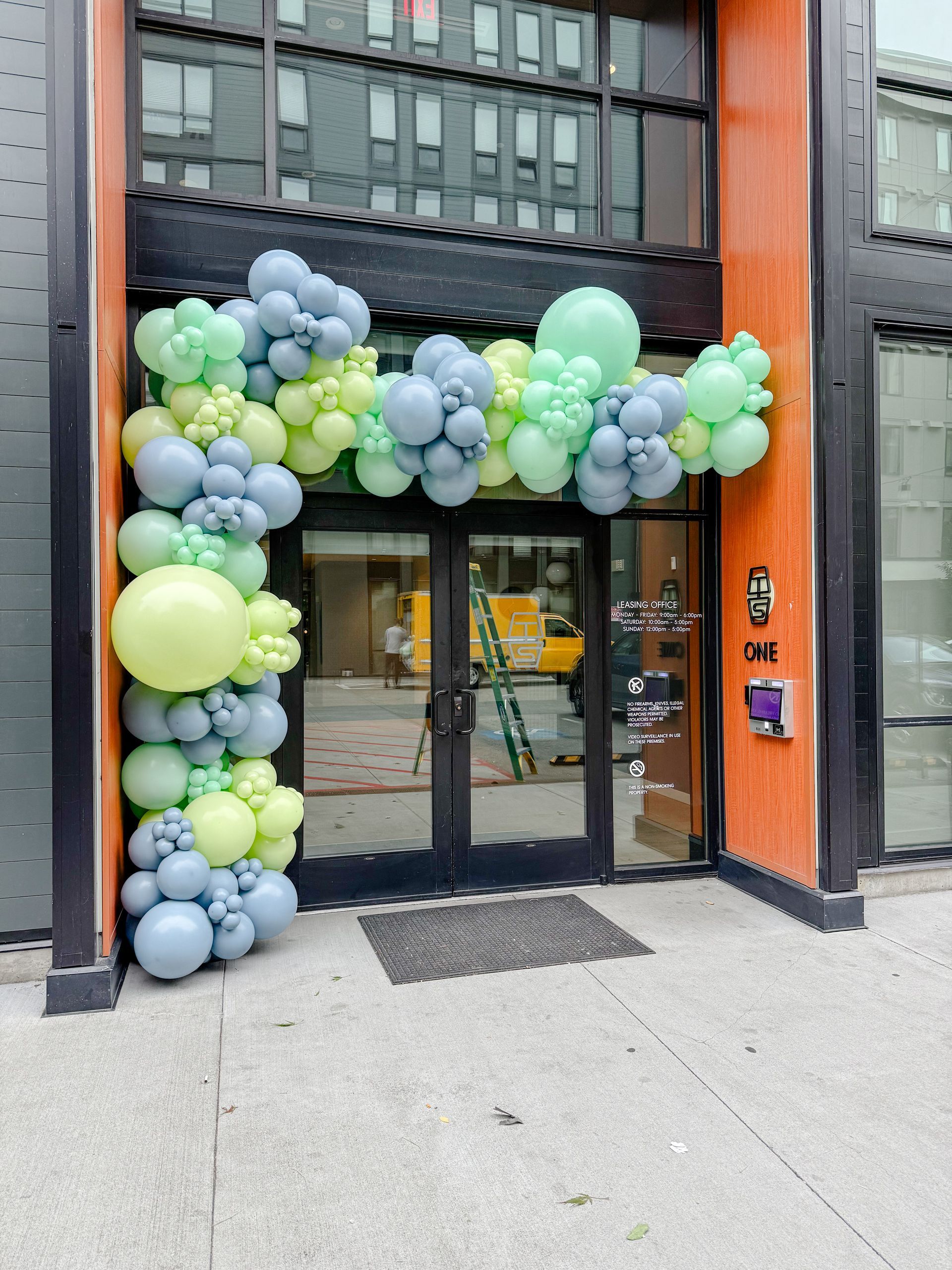 Doorway decorated with a balloon arch in shades of green and blue, leading into a building.