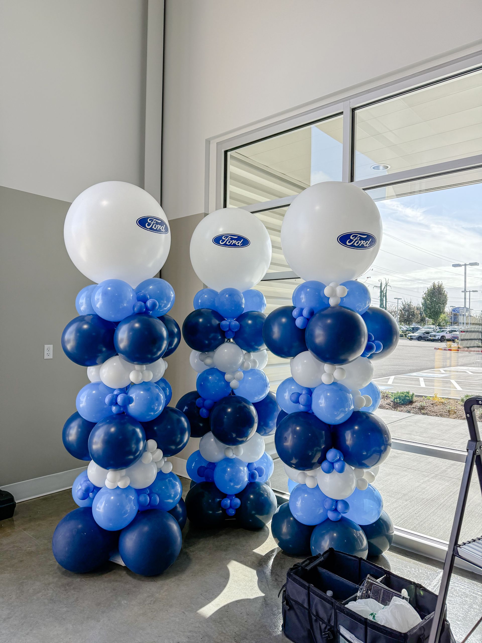 Three blue and white balloon columns topped with large white balloons, possibly for a business event.