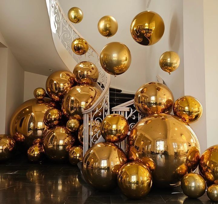 Gold balloons of varying sizes decorate a grand entrance with a winding staircase.