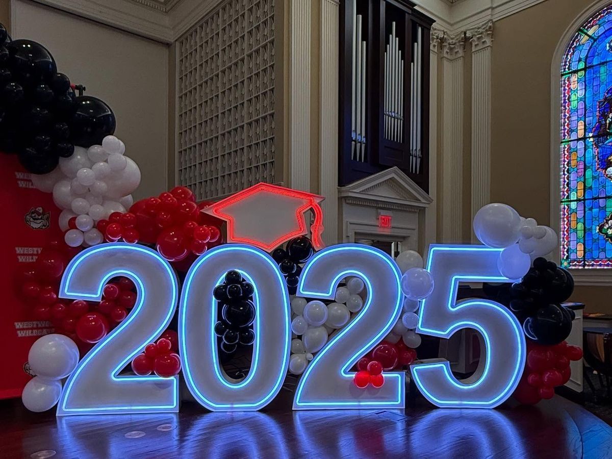 A large sign that says `` grad '' is surrounded by balloons in a room.