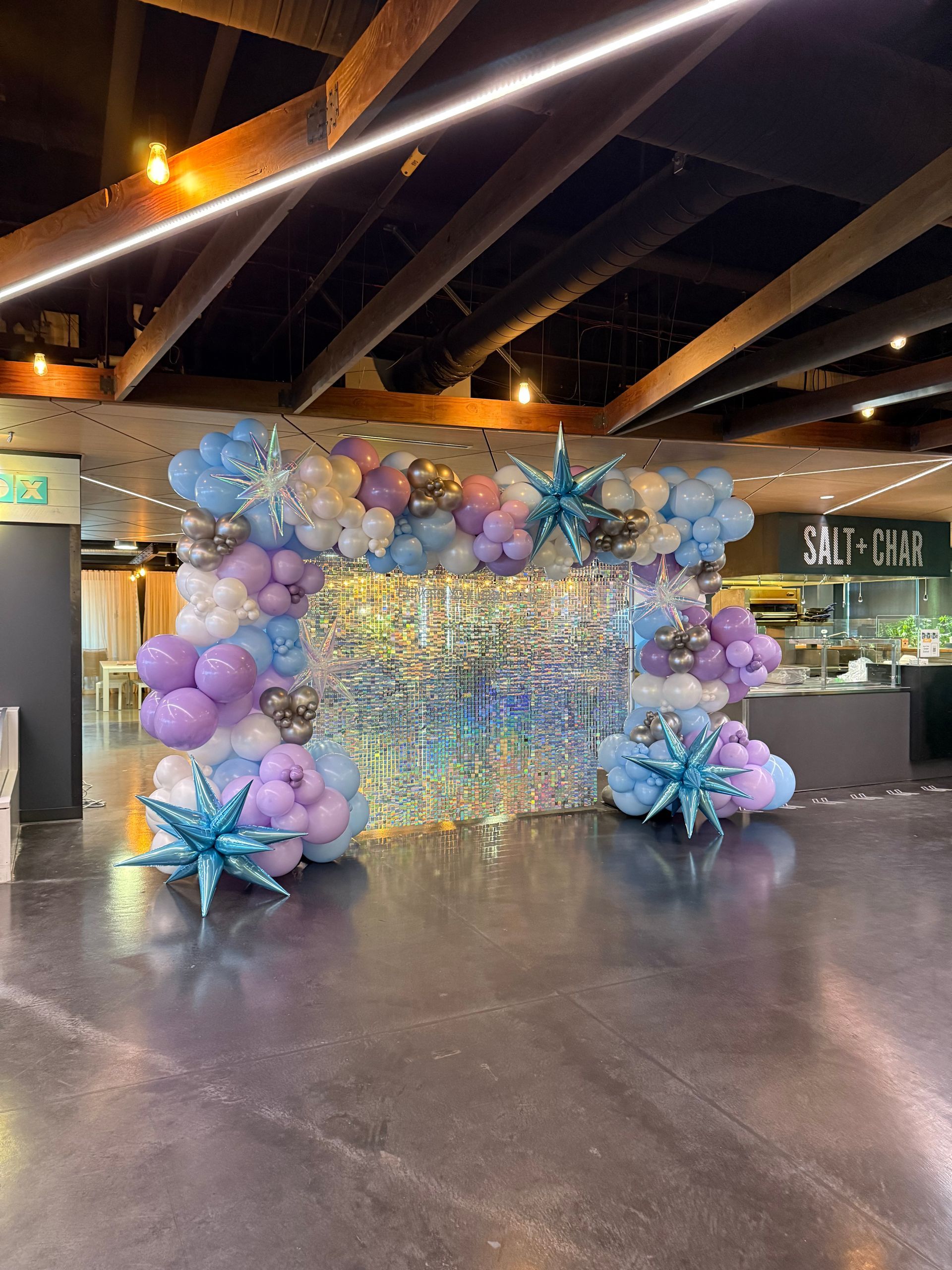 A festive display with balloons in blue, purple, and silver, a backdrop of shiny icicle-like strands.