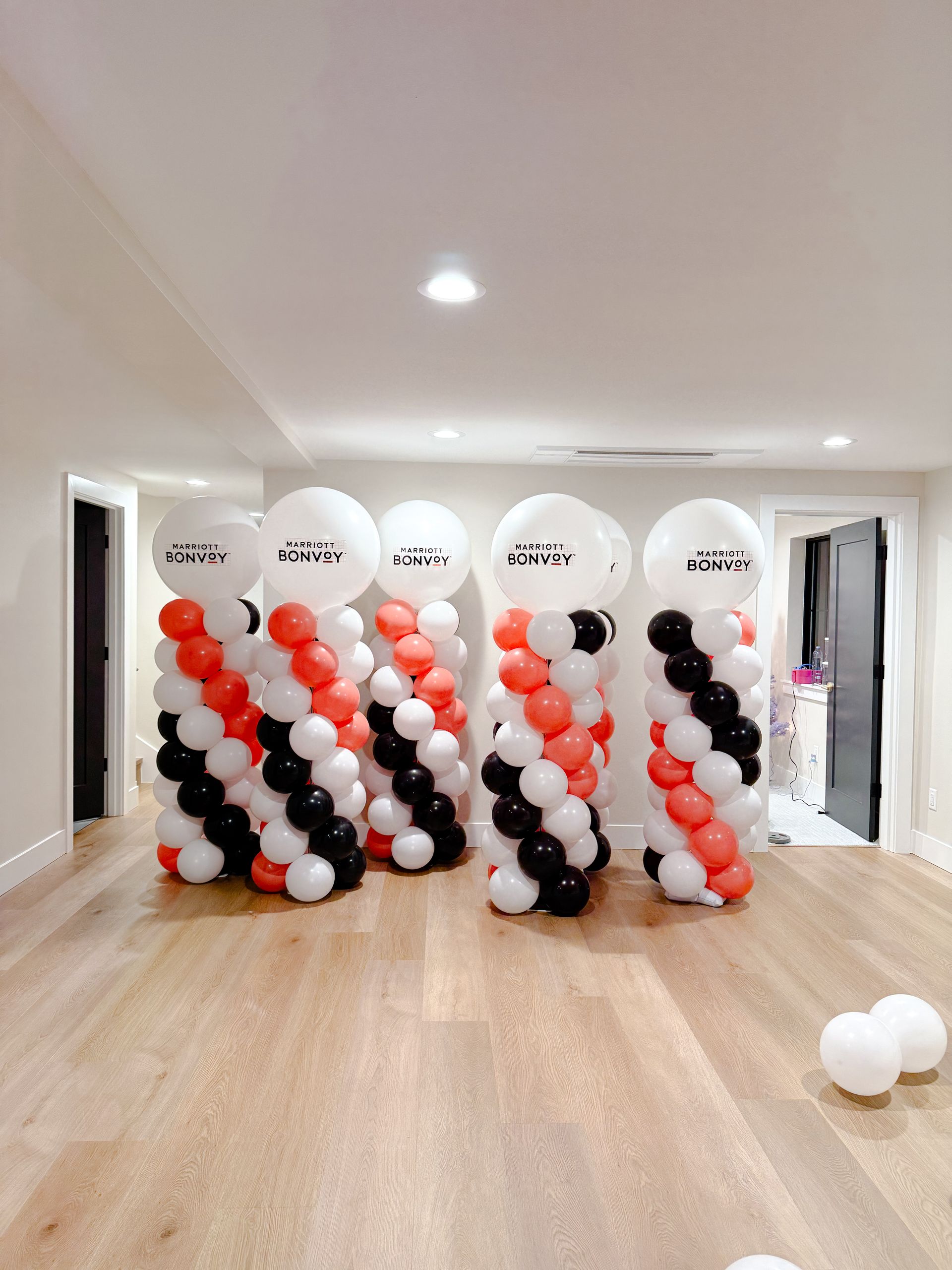 Five balloon columns with spiral patterns of black, white, and red balloons, topped with white balloons with black text.
