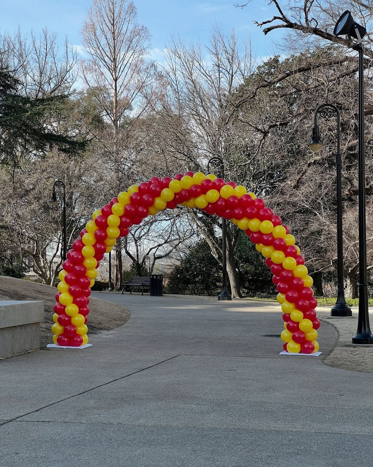 Red and yellow balloon arch over a pathway in a park.