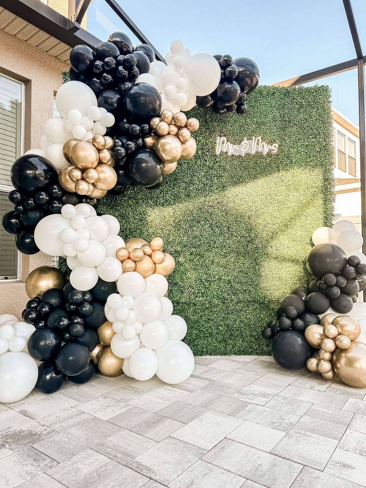 A wall covered in black , white , and gold balloons.