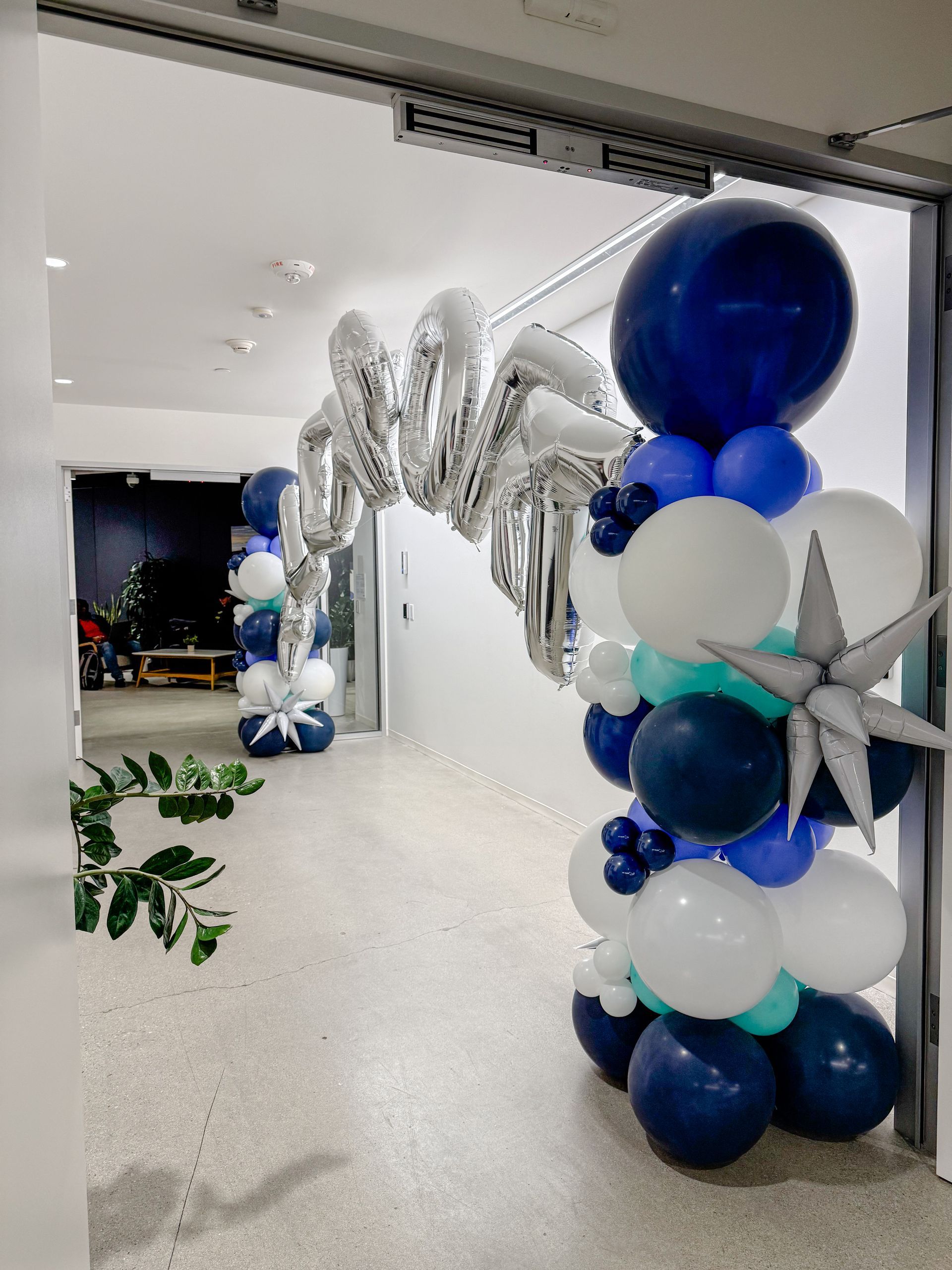 A hallway filled with blue , white , and silver balloons.