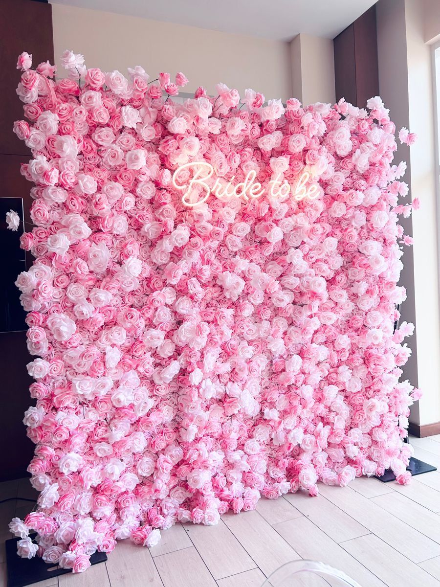 A wall of pink flowers with a neon sign that says bride to be.