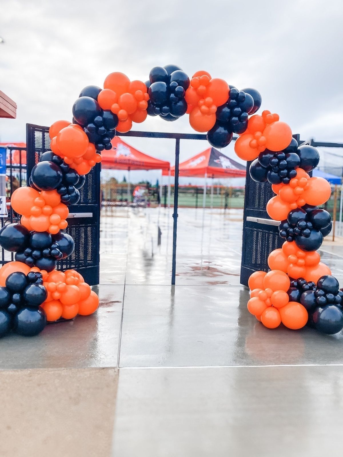 Orange and black balloon arch over a gate, likely for an event outdoors.