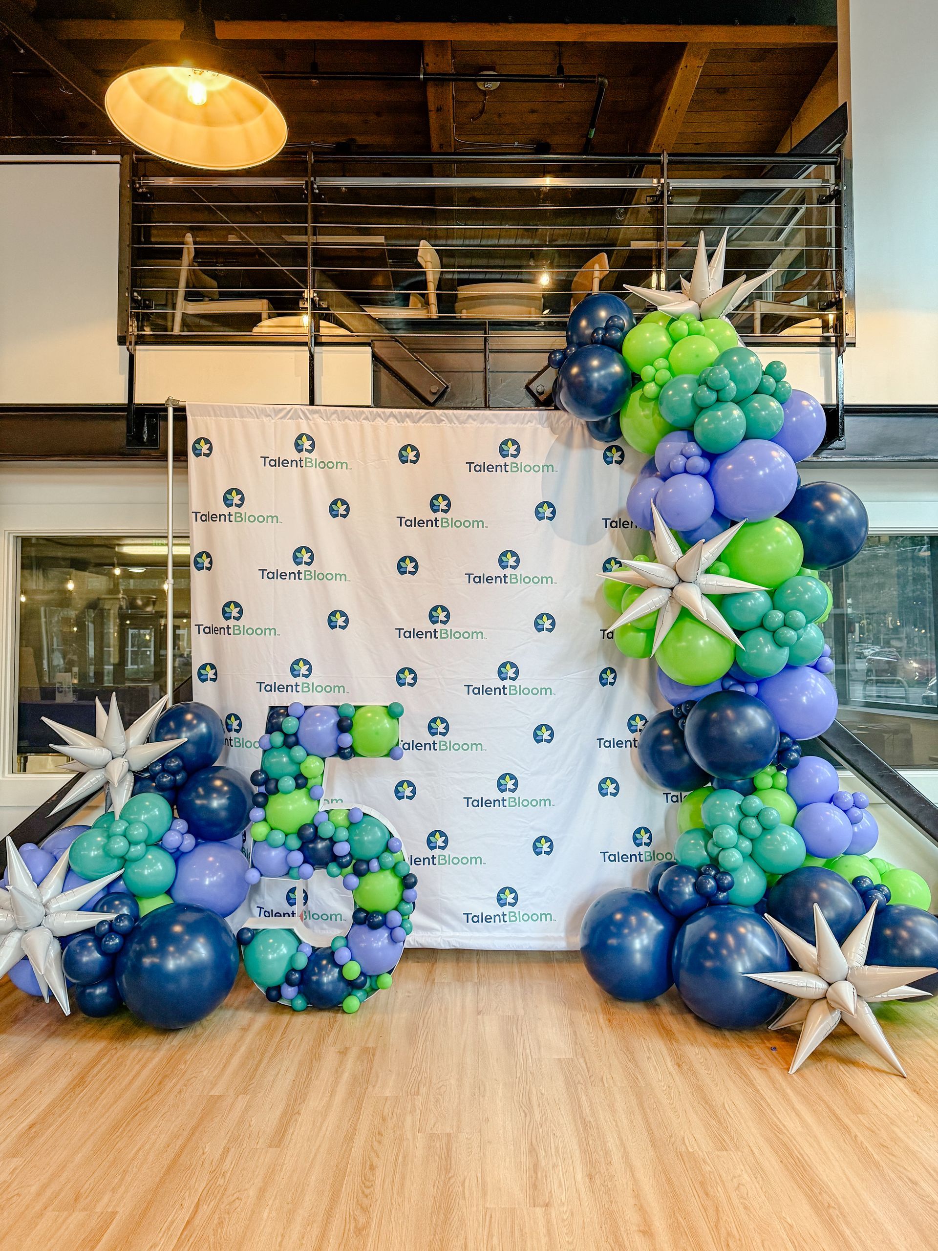 Balloon display in blue, green, and white beside a branded backdrop in an indoor venue