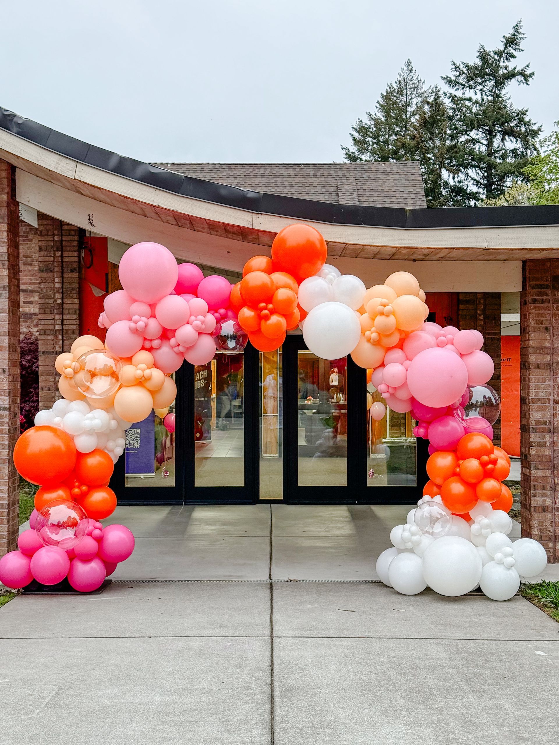 Balloon arch in pink, orange, and white frames a doorway.