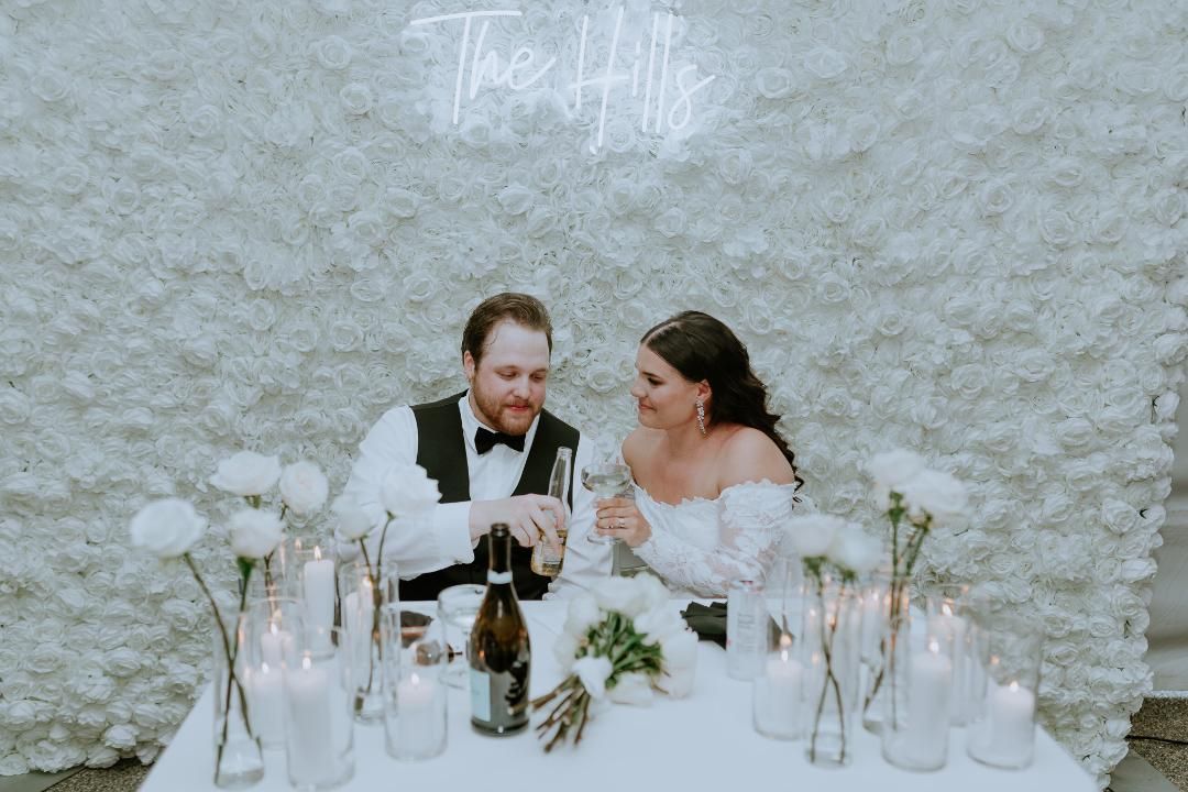 A bride and groom are sitting at a table with candles and flowers.