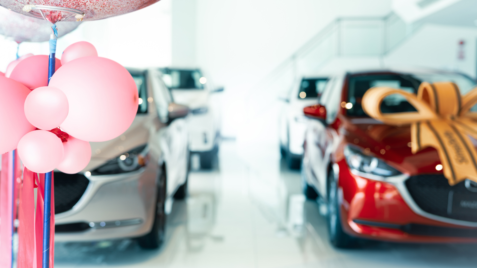 A row of cars are lined up in a showroom with balloons and bows.