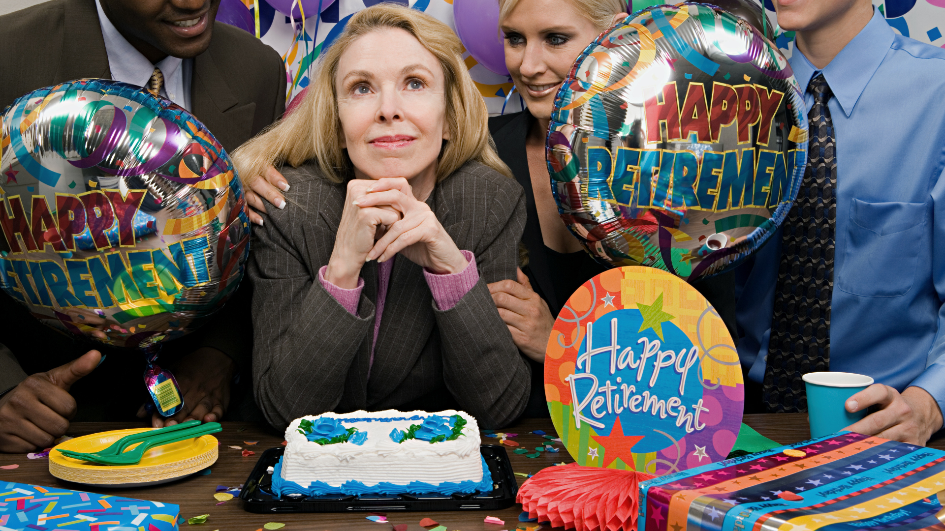 A woman sits at a table with balloons that say happy retirement