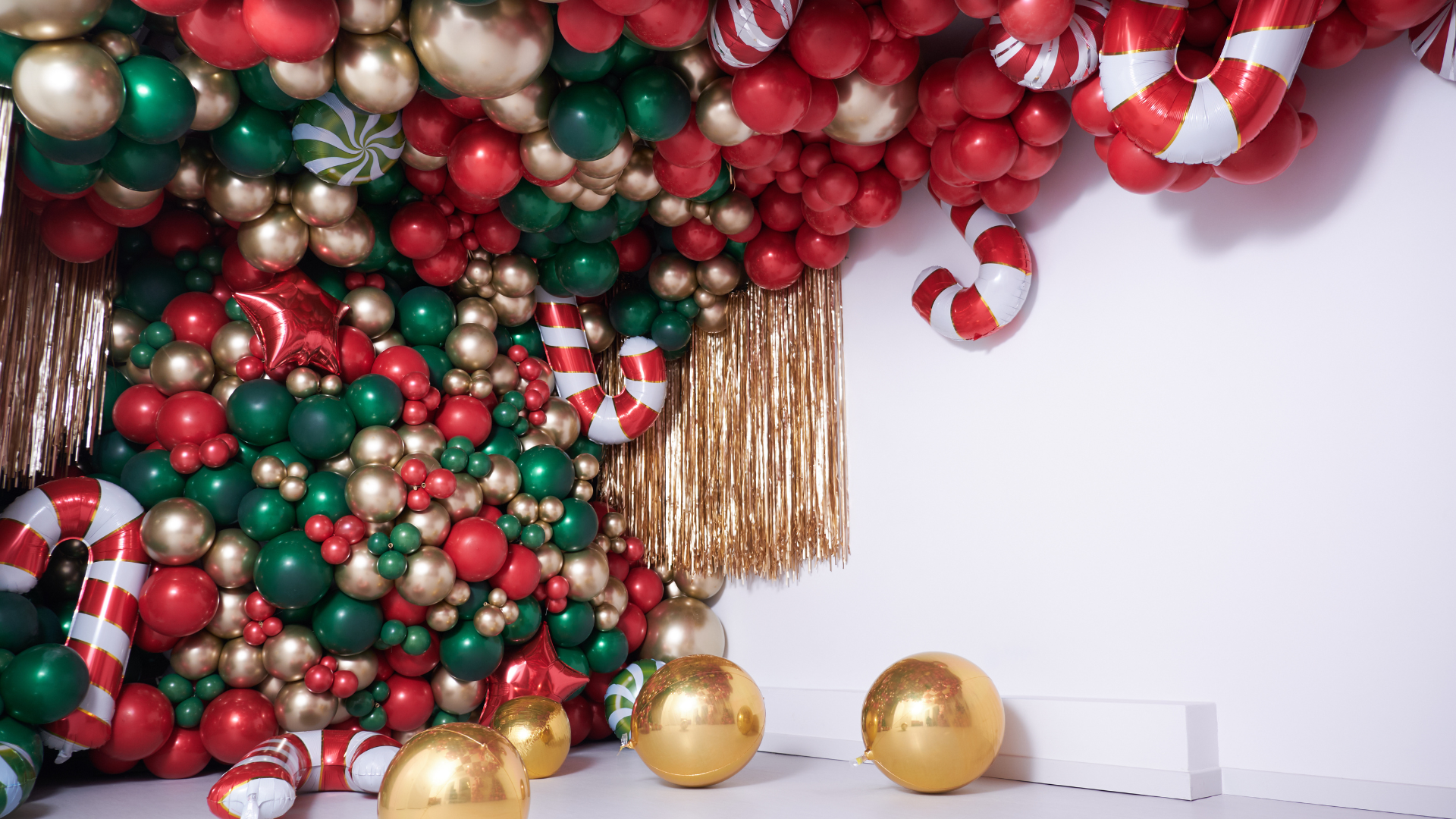 A wall filled with red , green and gold balloons and candy canes.
