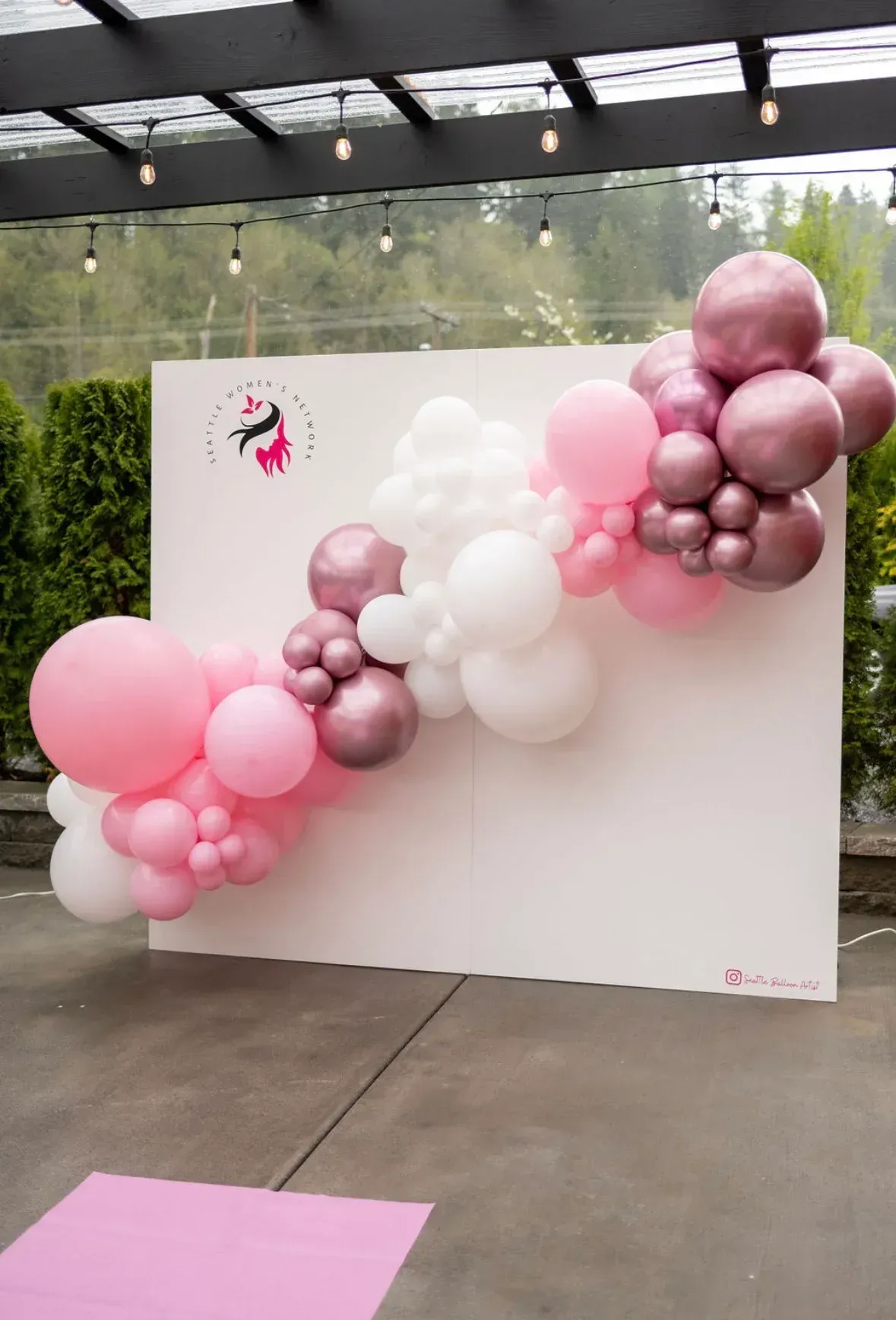A white wall with pink and white balloons on it.