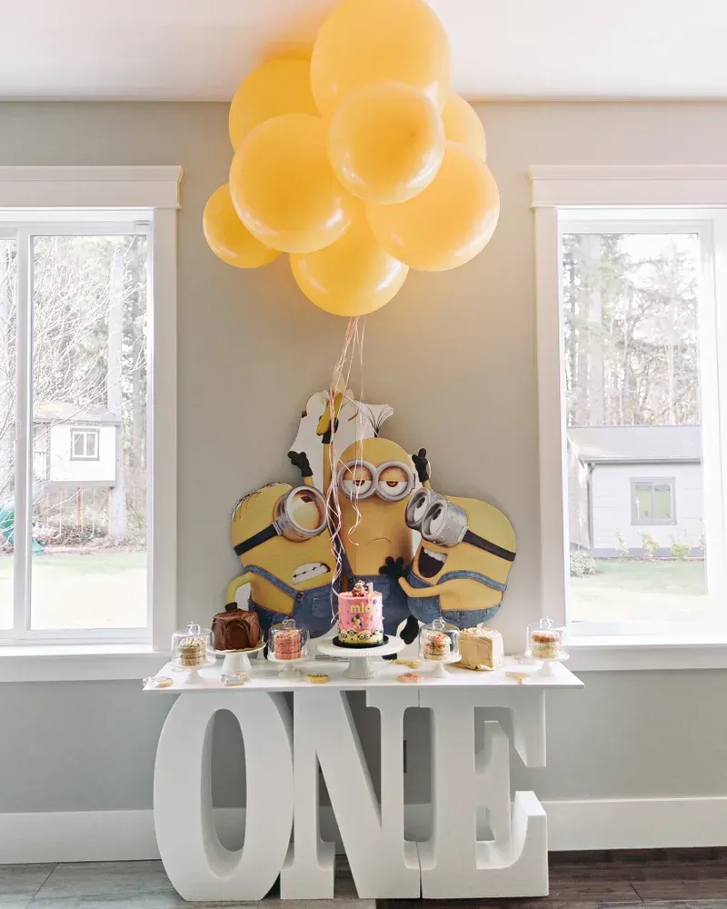 A table with balloons hanging from the ceiling and a sign that says one