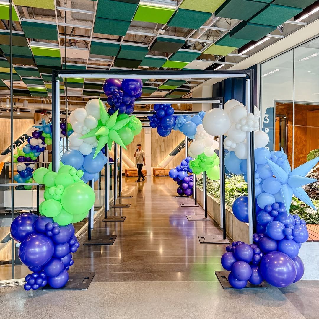 A hallway decorated with blue, white, and green balloons; person walking down the hall.