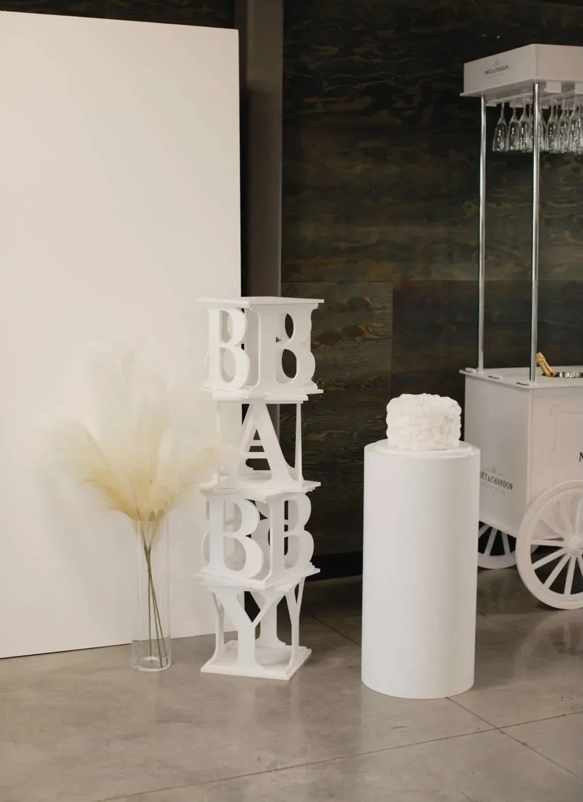 A baby shower decoration with white letters and a white cart.