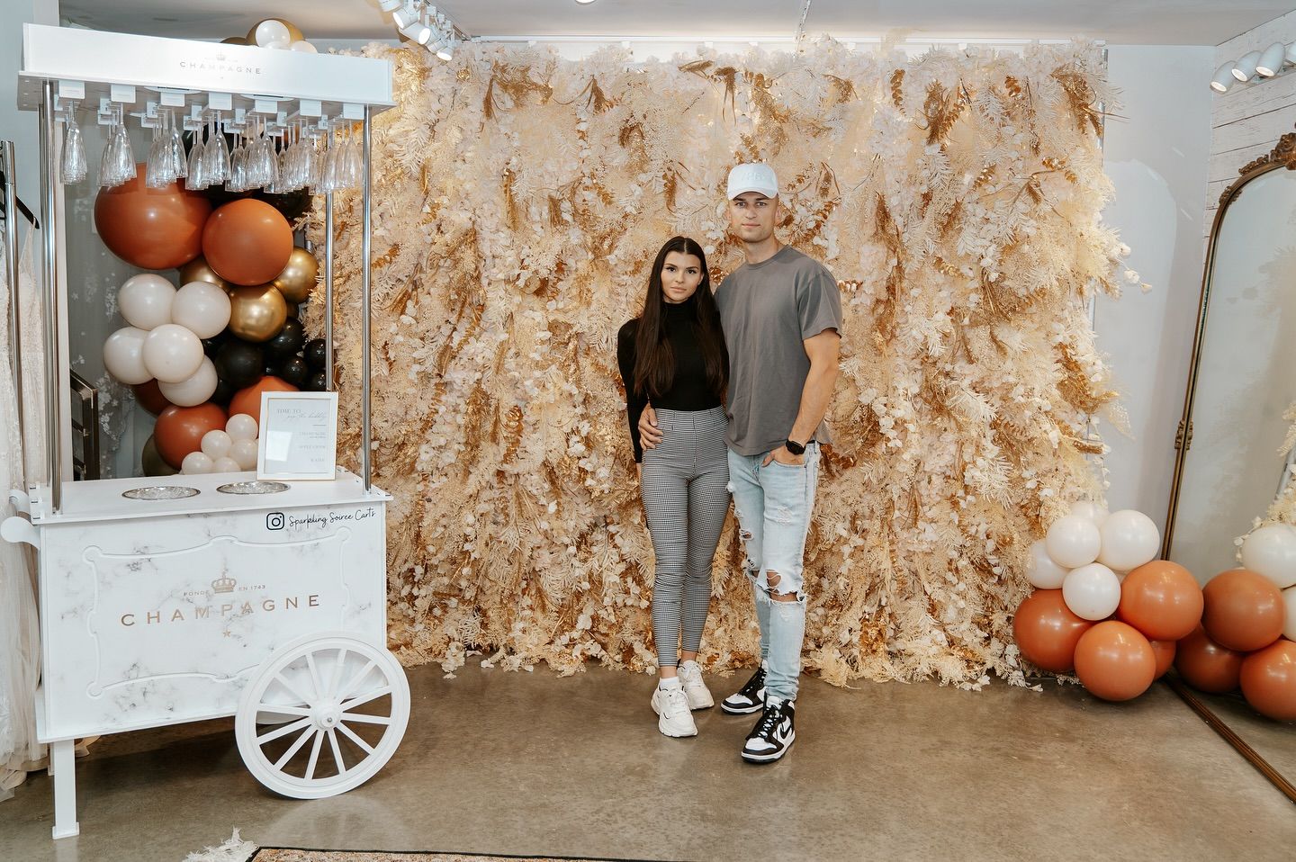 A man and a woman are standing in front of a cart filled with balloons.