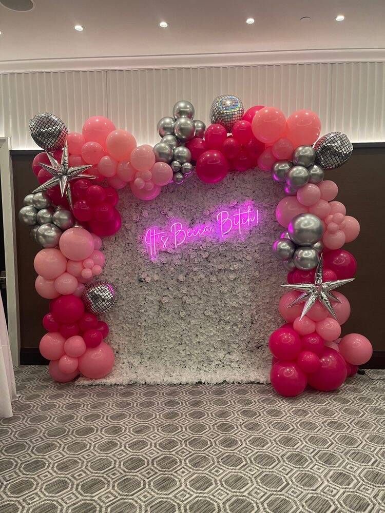 A room decorated with pink and silver balloons and a neon sign.