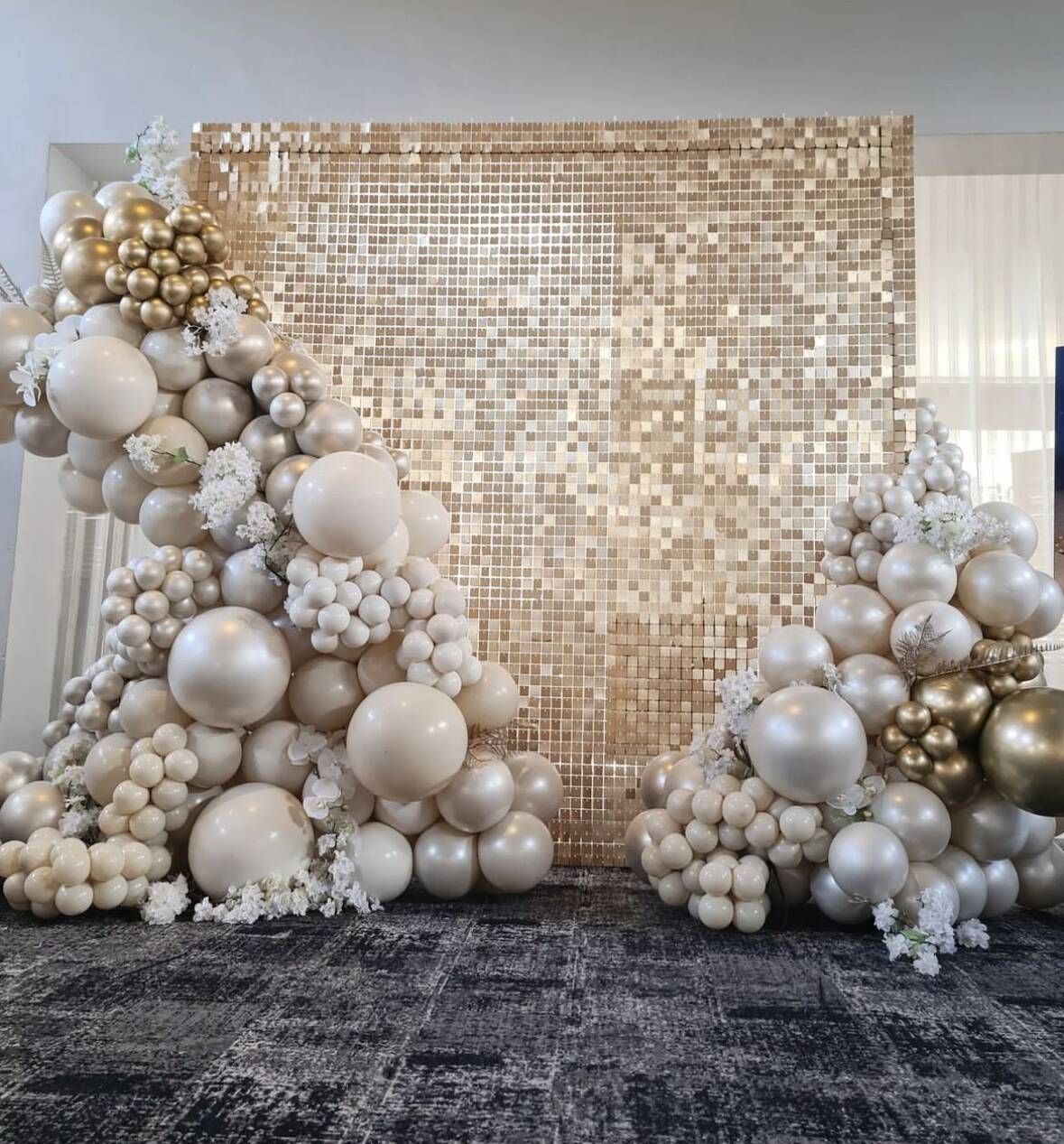 A wall covered in white and gold balloons and flowers.