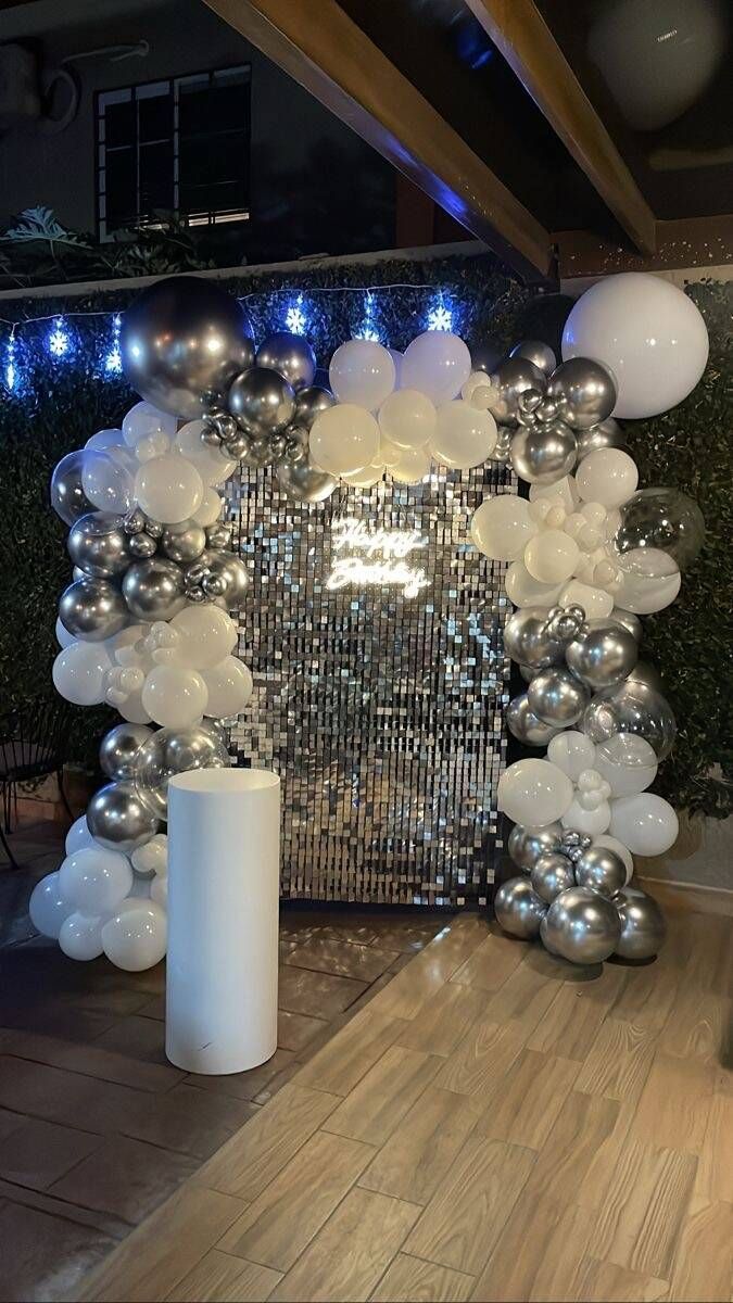 A room decorated with silver and white balloons and a white pillar.