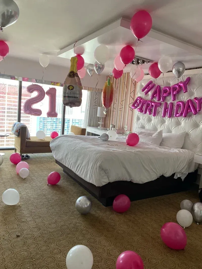 A bedroom decorated for a 21st birthday with balloons and a bottle of champagne.