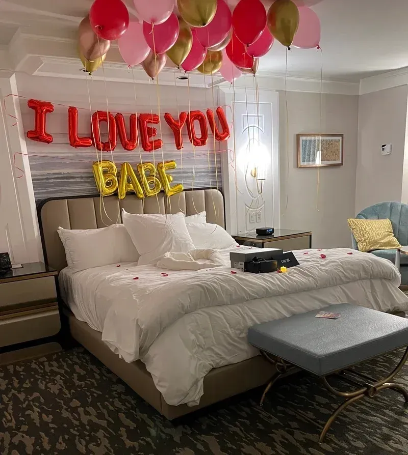 A bedroom with a bed and balloons that say i love you babe