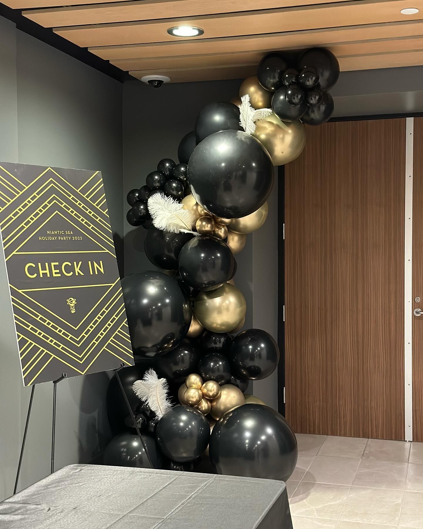 A bunch of black and gold balloons are hanging from the ceiling in a room.