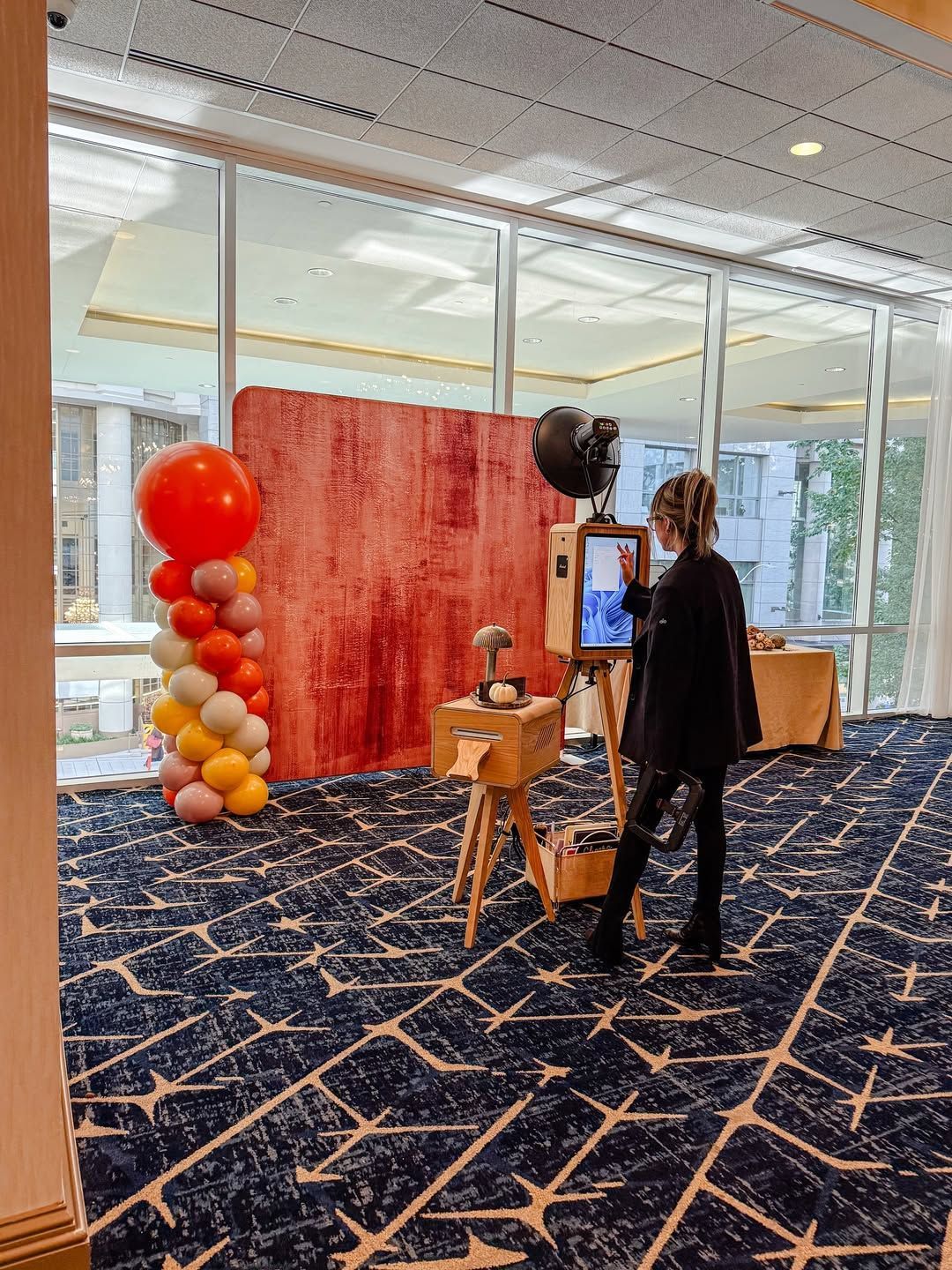 Booth with red backdrop and balloon column at an event, with a person adjusting a Microsoft tablet.