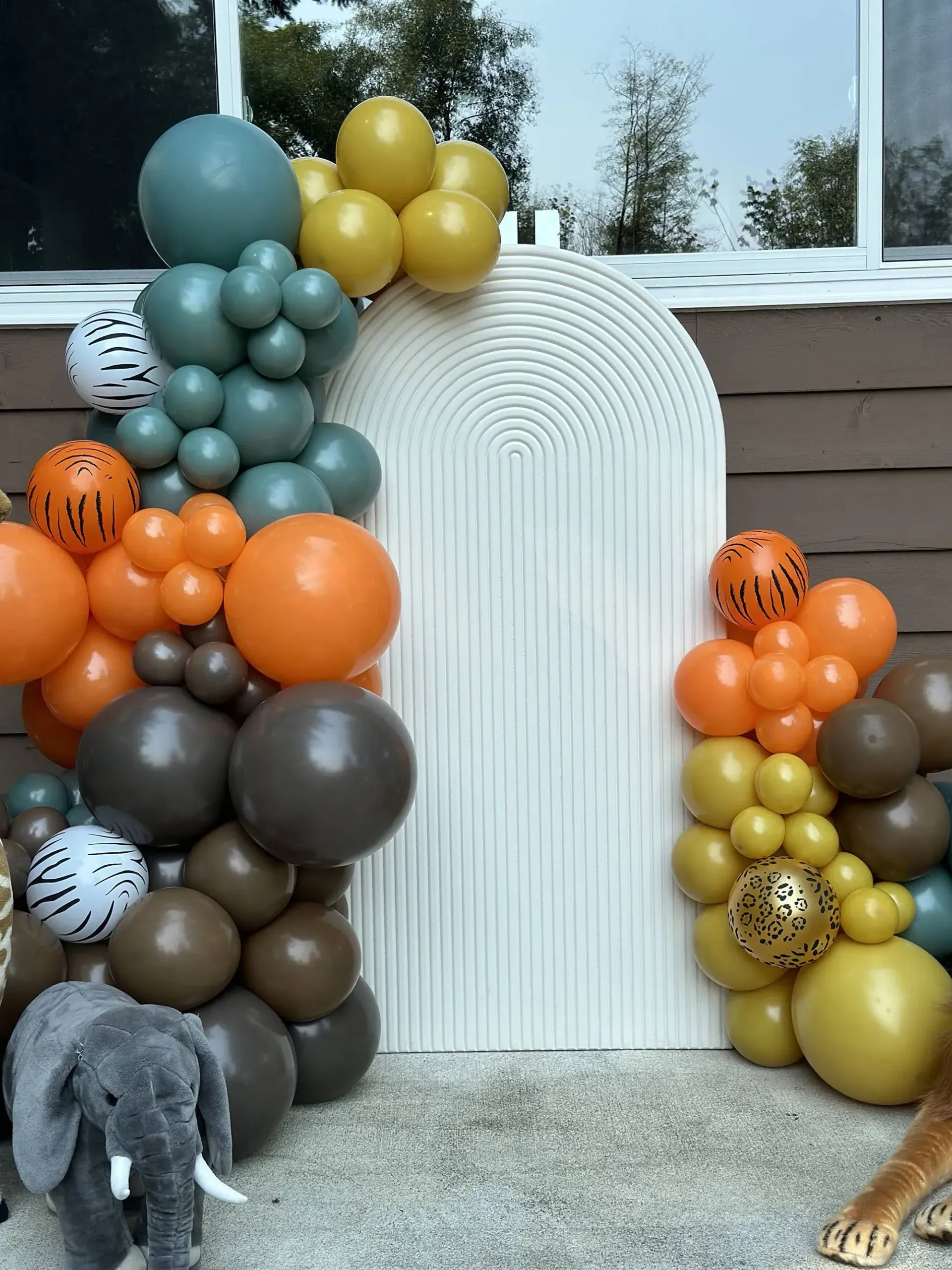 A stuffed elephant is standing in front of a balloon arch.