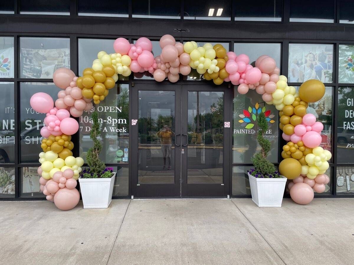 A pink and gold balloon arch is in front of a building.