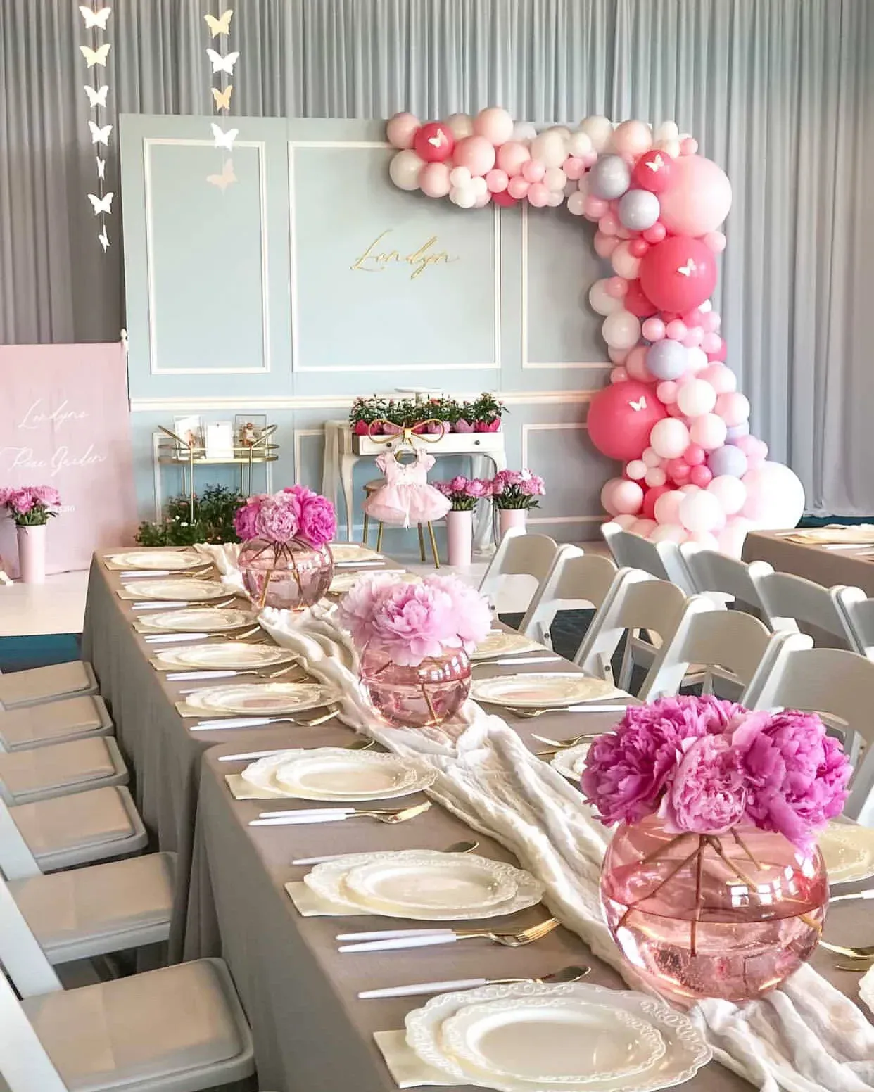 A long table with plates , utensils , vases of flowers and balloons.