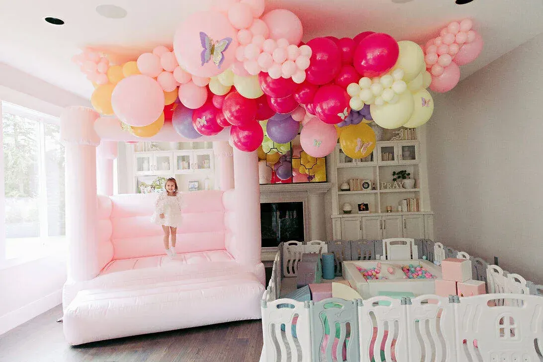 A girl is standing in a room with balloons hanging from the ceiling.