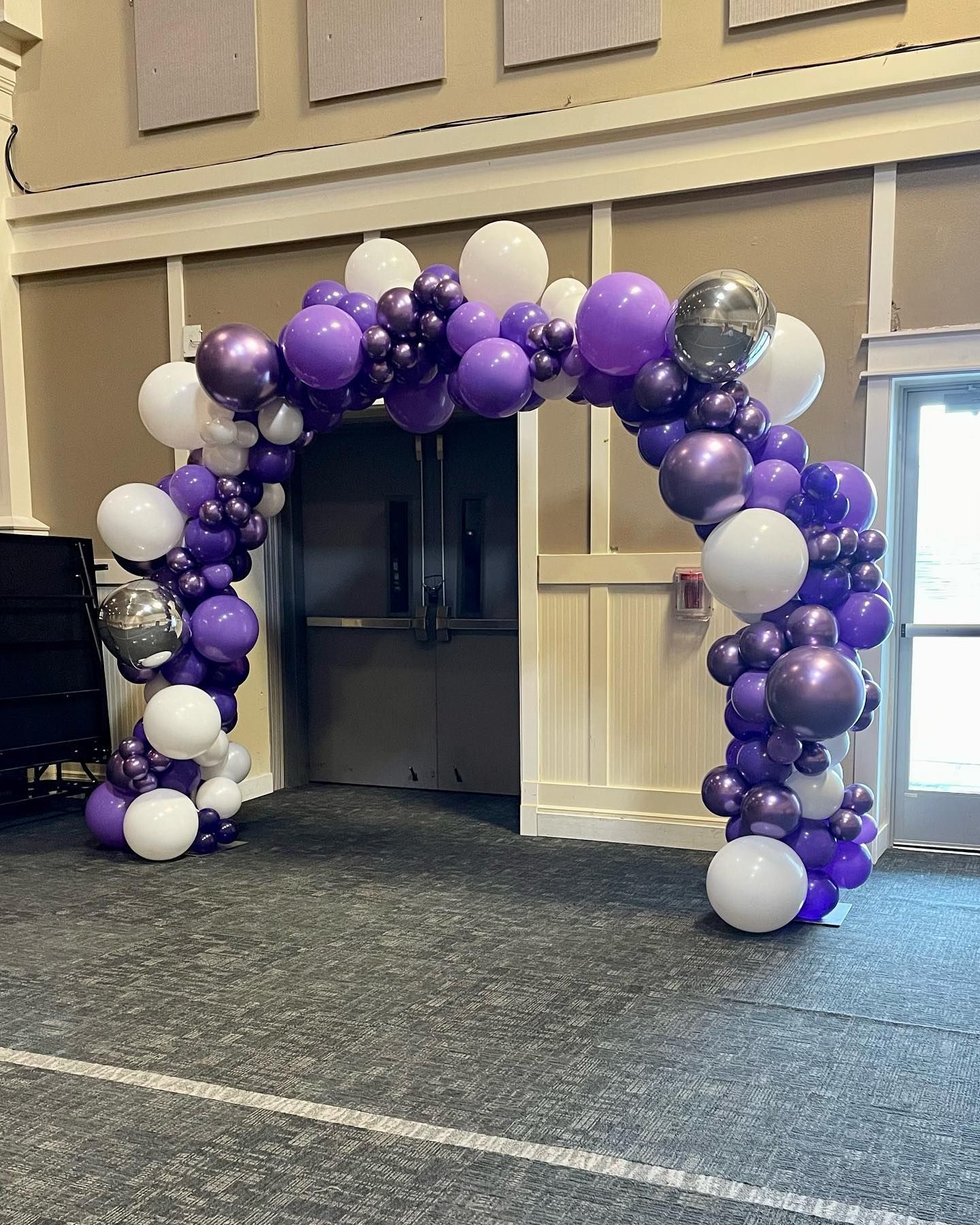 A large arch made of purple and white balloons in a room.