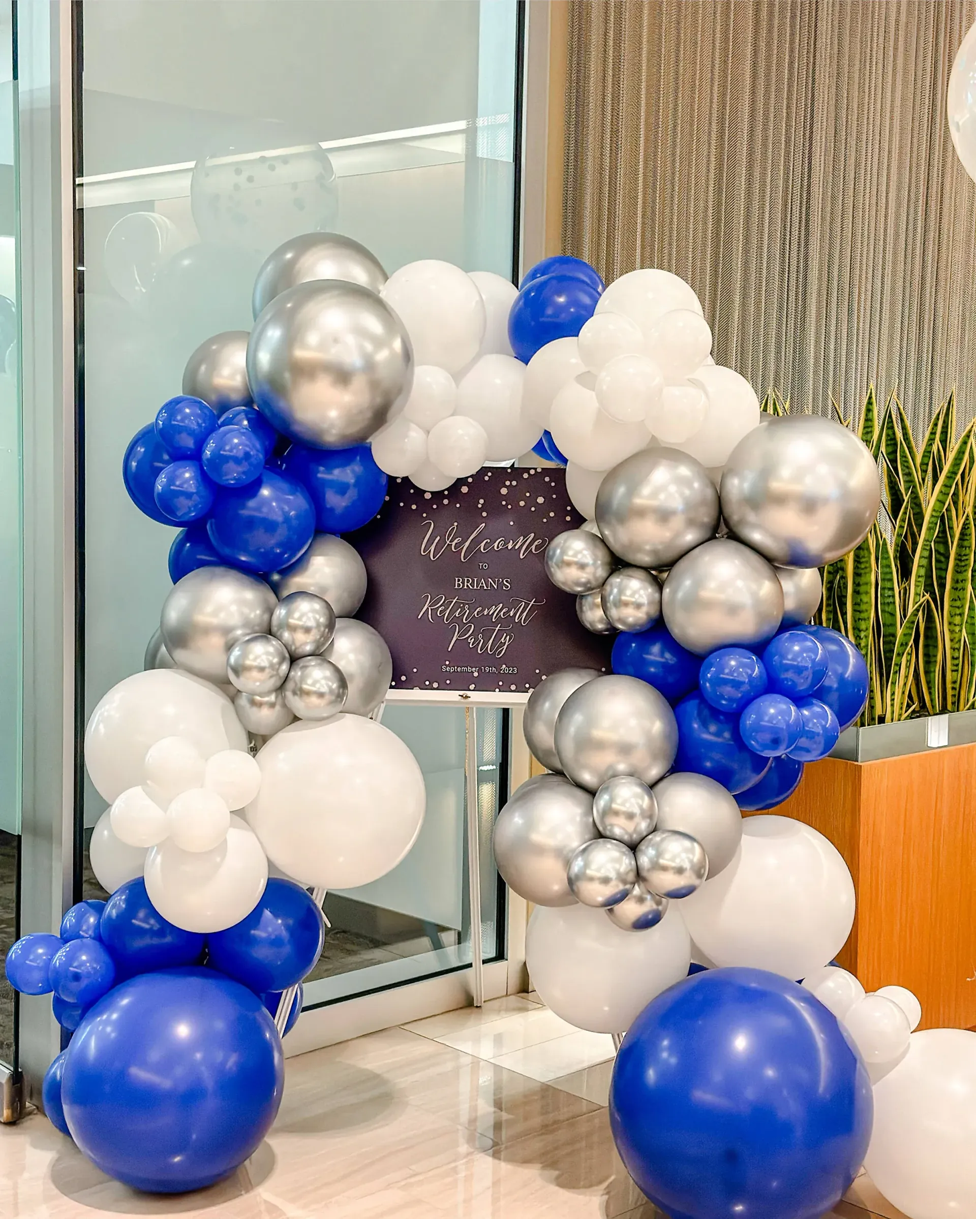 A bunch of blue , white and silver balloons are sitting on the floor.