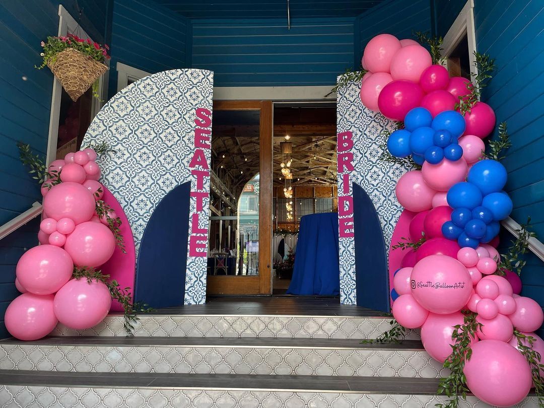 A bunch of pink and blue balloons are sitting on the steps of a building.