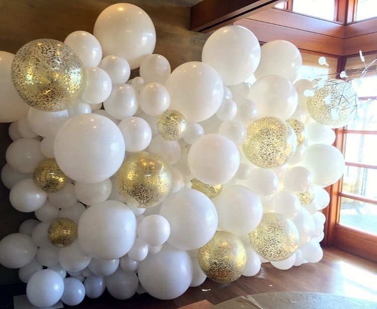 A wall of white and gold balloons in a room