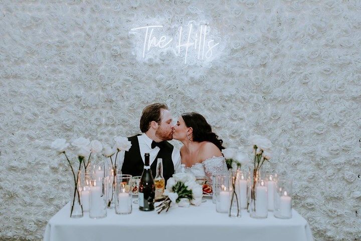 A bride and groom are kissing at a table with candles and wine.