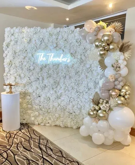 A wall of white flowers and balloons with a neon sign that says the thunders.