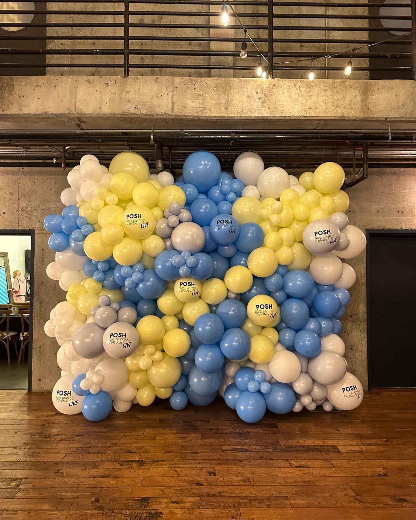 A wall of blue and yellow balloons on a wooden floor.