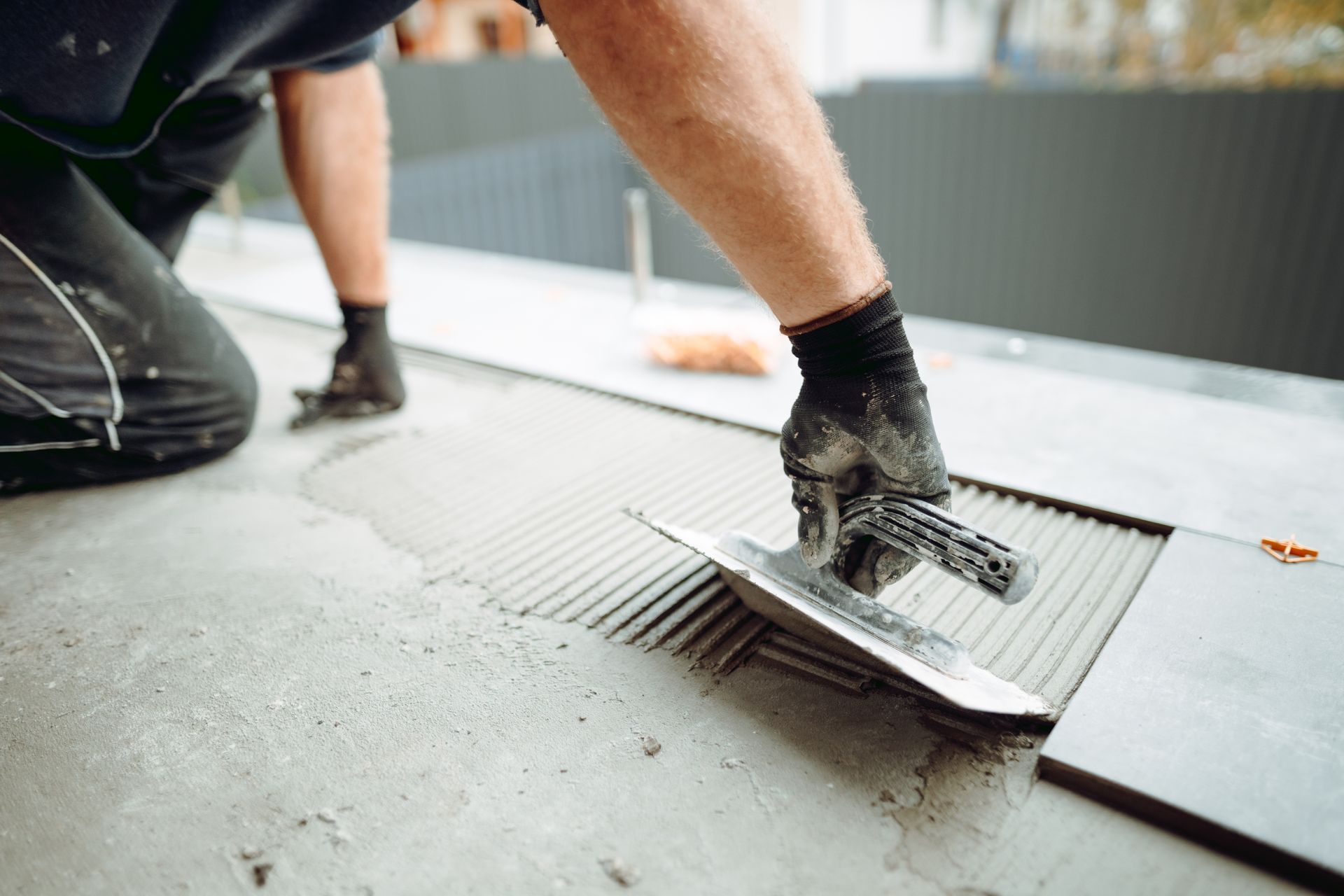 Person using a notched trowel to spread adhesive for tiling a surface.