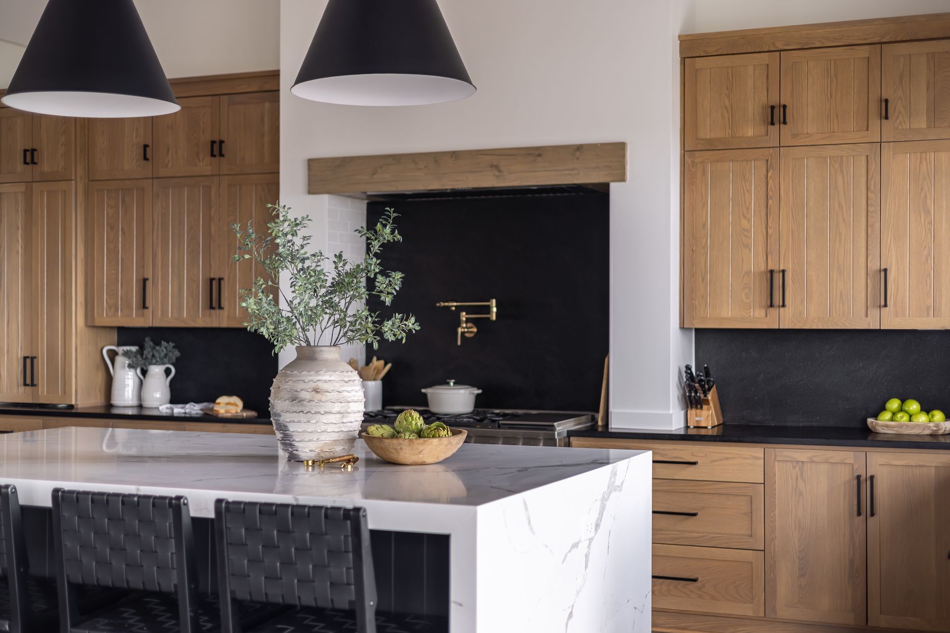 Kitchen with light wood cabinets, black backsplash, white countertop island, and black pendant lights.
