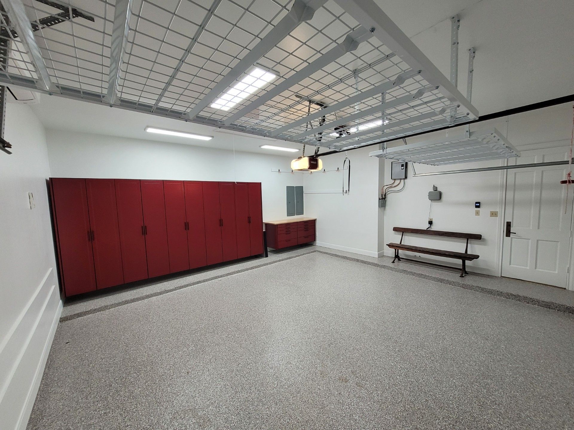 Spacious garage with red lockers, gray speckled floor, and wall-mounted workbench under bright ceiling lights