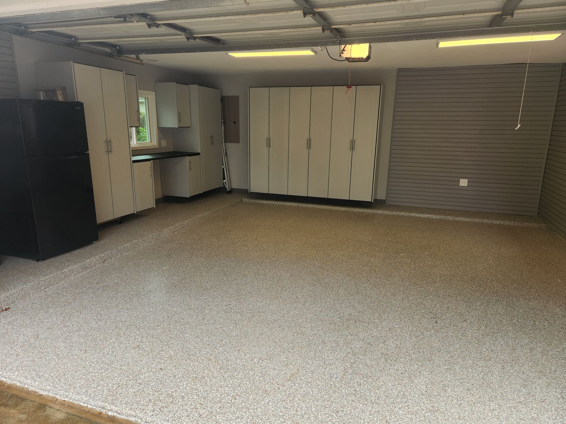 Empty garage with a white storage cabinet, sink, black refrigerator, and closed roll-up door